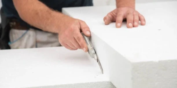 DIY installer trimming polystyrene PS wall panel with utility knife to fit around electrical outlet opening during interior wall panel installation showing ease of cutting lightweight foam wall covering material DIY installer trimming polystyrene PS wall panel with utility knife to fit around electrical outlet opening during interior wall panel installation showing ease of cutting lightweight foam wall covering material